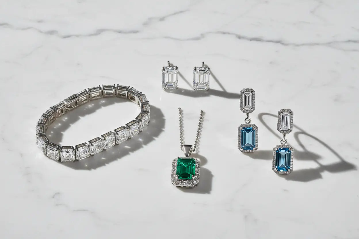 Emerald cut diamond tennis bracelet, solitaire stud earrings, emerald gemstone halo pendant, and art deco dangle earrings — emerald jewelry collection at Bijoux NYC Direct