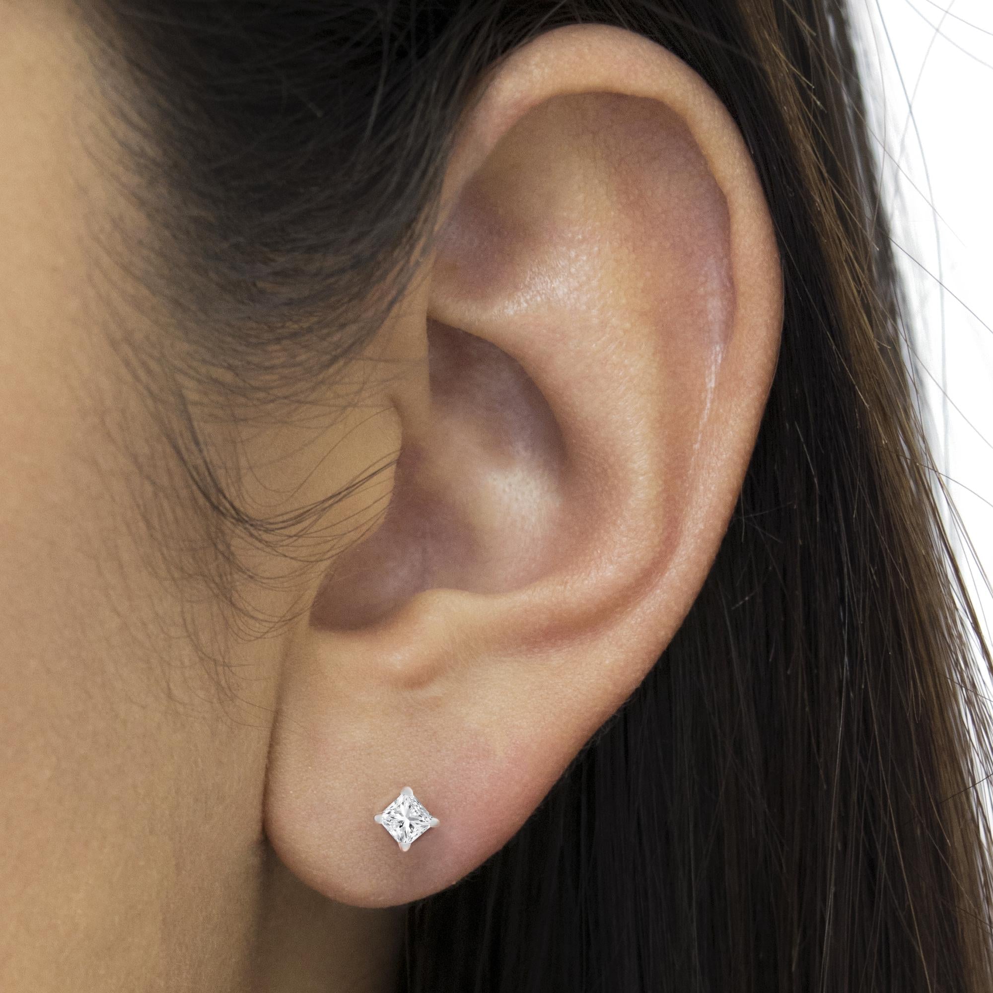 Close-up of an ear wearing a diamond stud earring with dark hair in the background