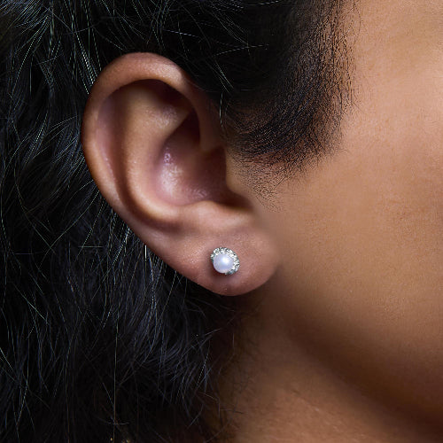 Close-up of an ear wearing a pearl stud earring with dark hair.