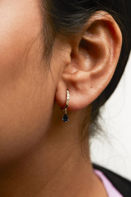 Close-up of an ear wearing a gold hoop earring with a blue gemstone.
