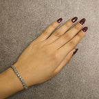 Hand with maroon nail polish wearing a gold diamond bracelet on a beige background