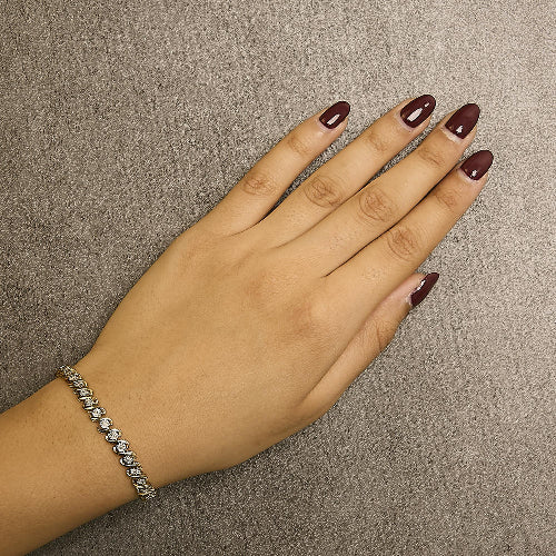 Hand with maroon nail polish wearing a gold diamond bracelet on a beige background