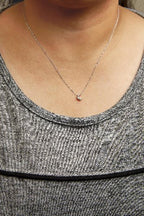 Necklace with a small pendant worn by a person in a gray tank top.