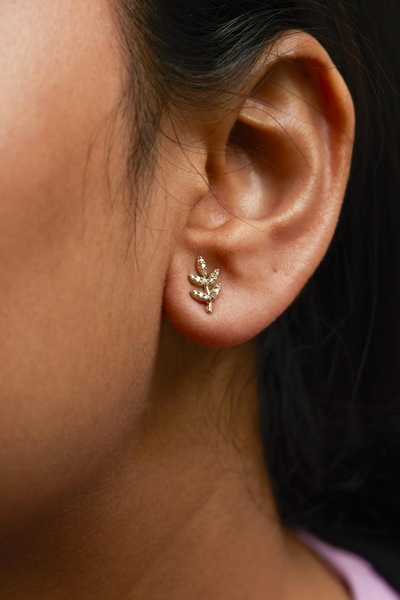 Close-up of an ear wearing a gold earring with a leaf design.