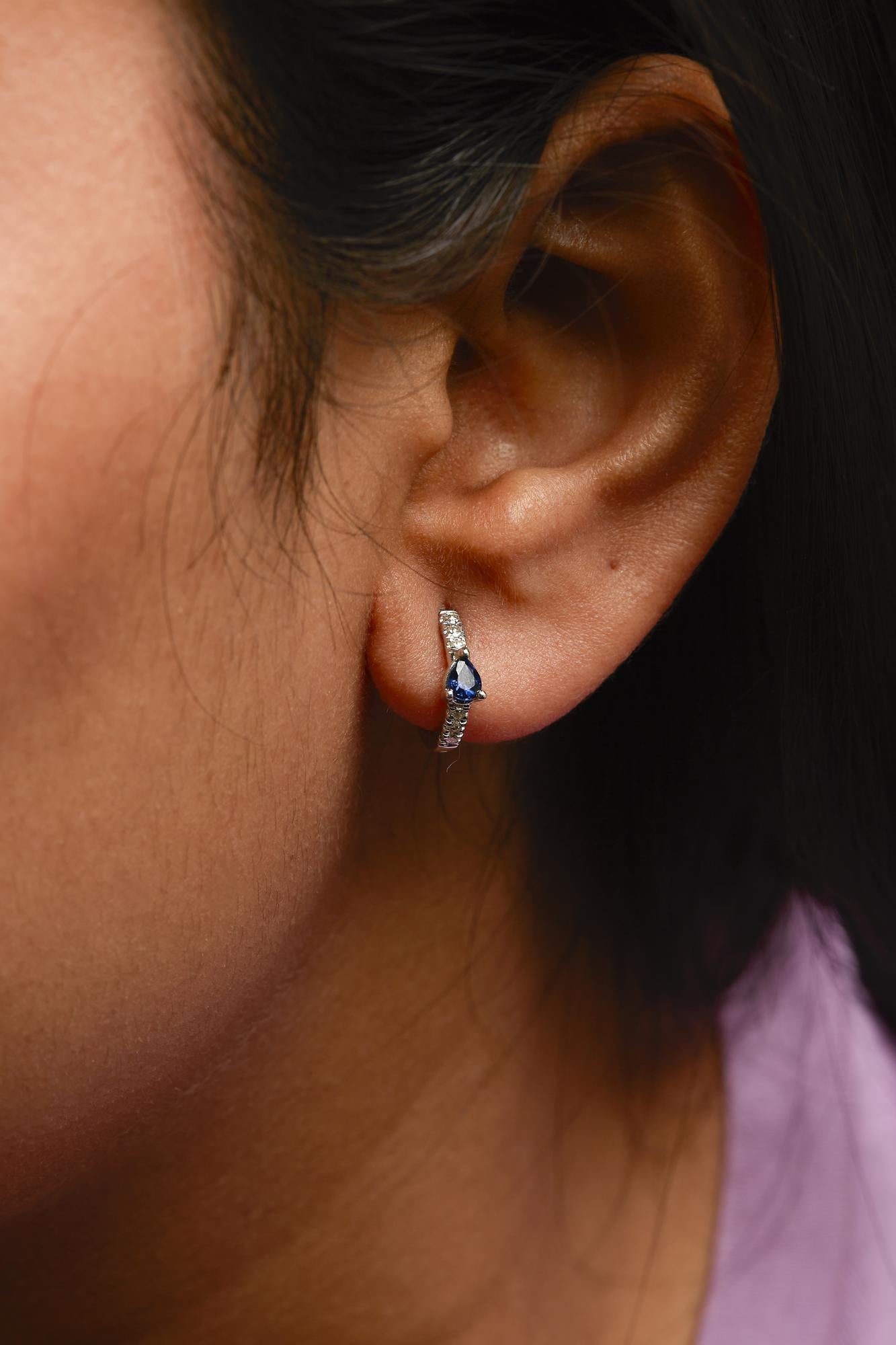 Close-up of an ear wearing a blue gemstone earring with a blurred background