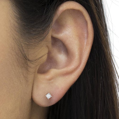 Close-up of an ear wearing a diamond stud earring with dark hair in the background