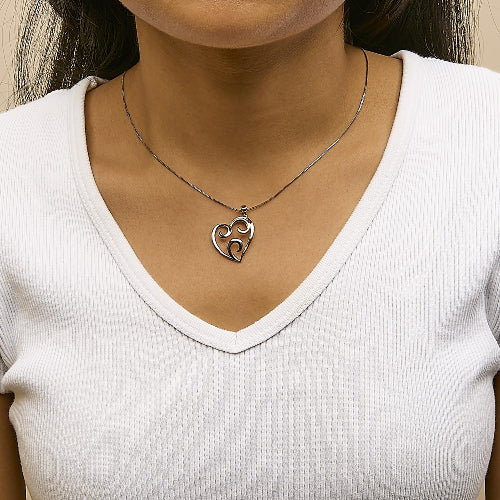 Silver necklace with a heart-shaped pendant worn by a person in a white shirt.