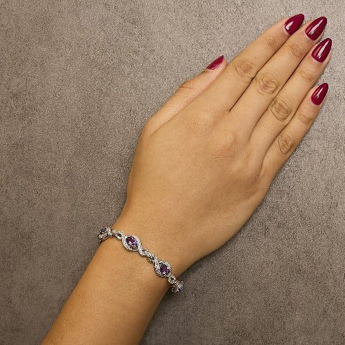 Hand wearing a silver bracelet with purple stones on a brown background