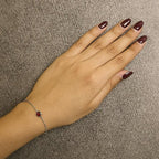 Hand with maroon nail polish wearing a silver bracelet on a beige background