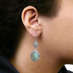 Close-up of an ear wearing a silver earring with a green gemstone.