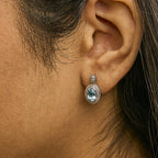 Close-up of an ear wearing a diamond earring with a blue gemstone.