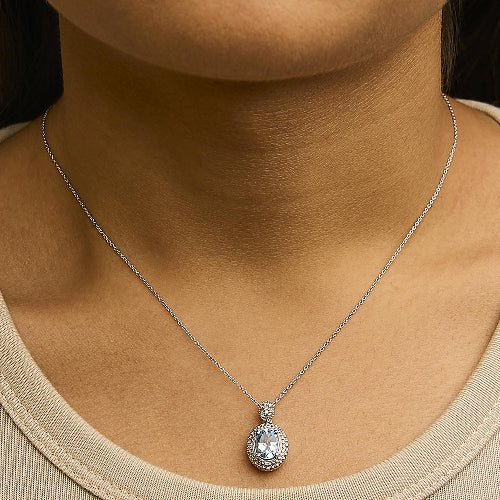 Silver necklace with a pendant on a person wearing a beige top.