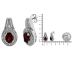 Silver earrings with red gemstones and a ruler for scale on a white background