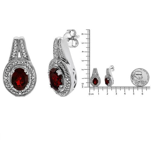 Silver earrings with red gemstones and a ruler for scale on a white background