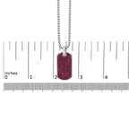 Dog tag pendant with pink glittery design on a chain, shown with a ruler for scale.