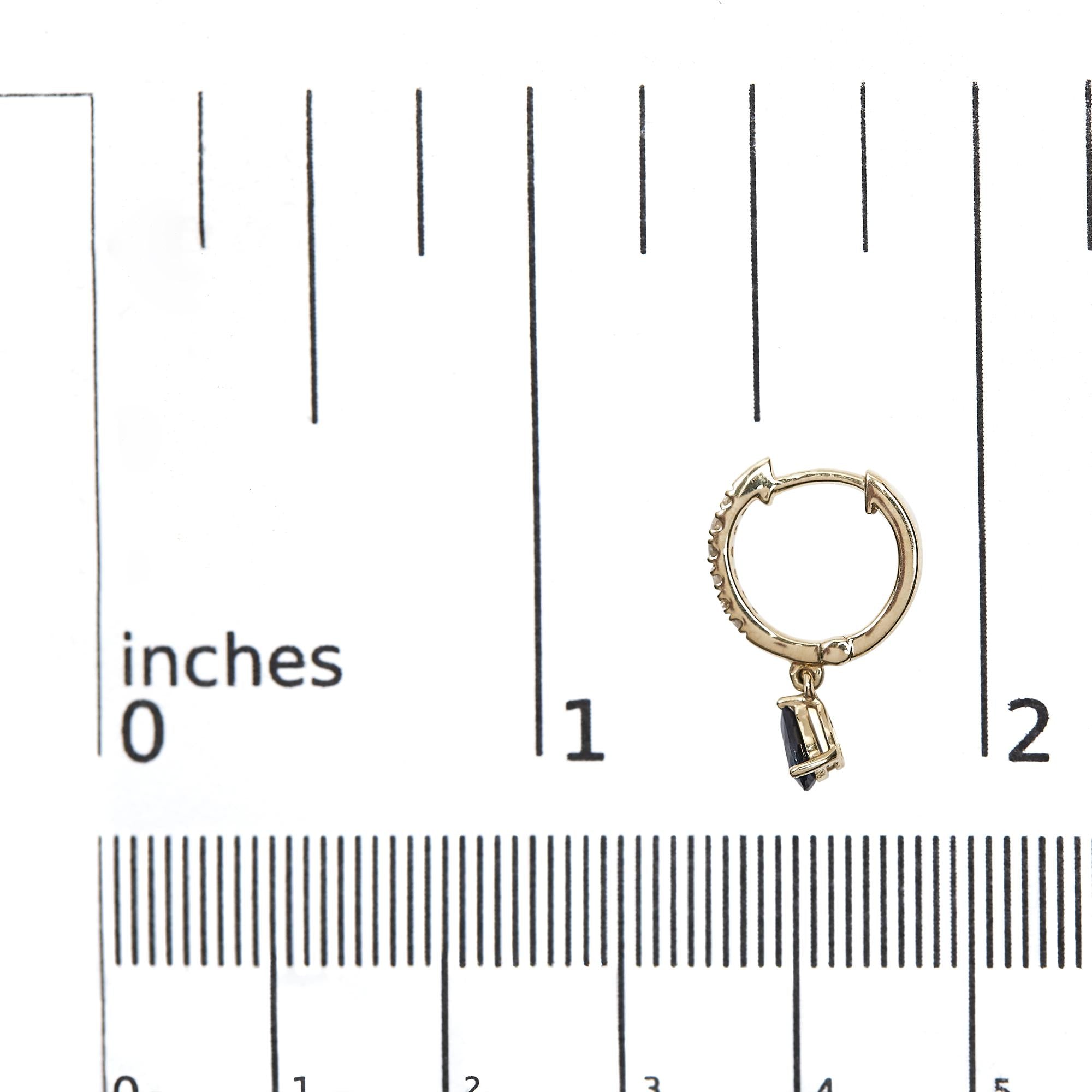 Gold hoop earring with a small pendant on a ruler for scale.