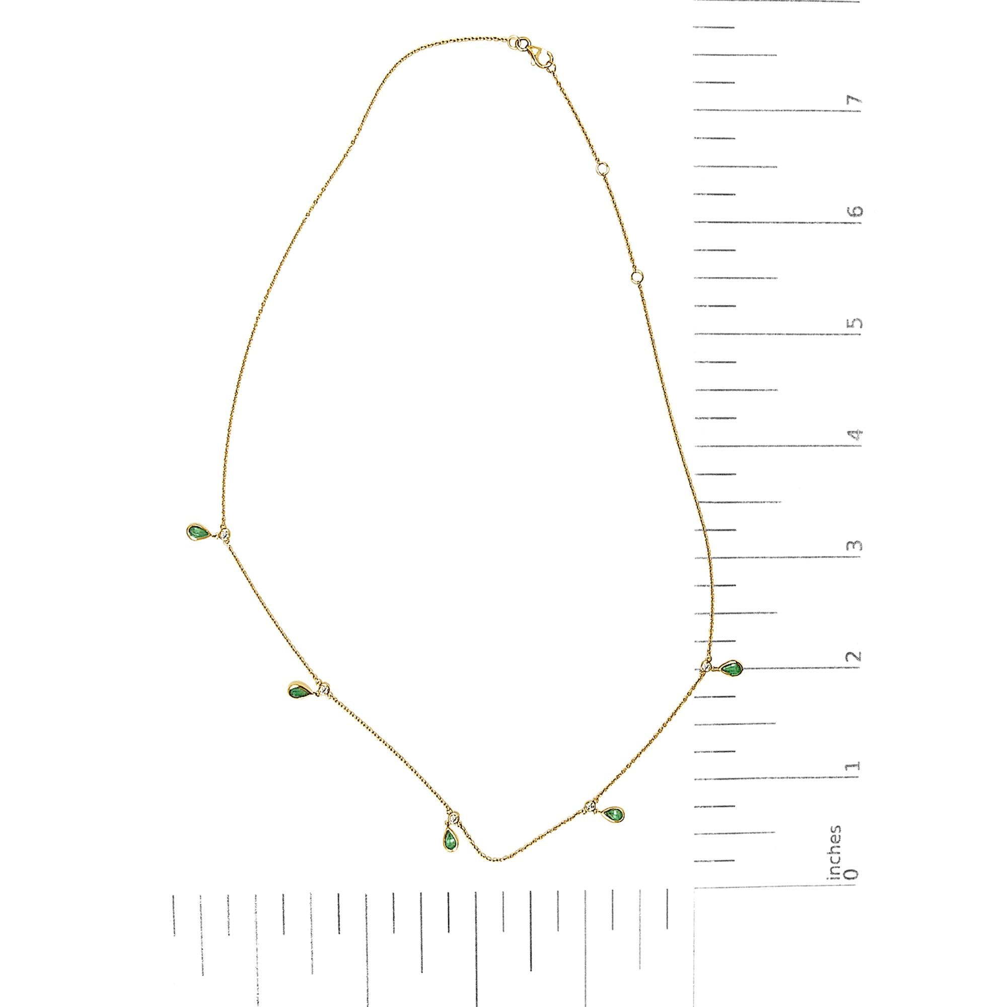 Gold necklace with green gemstones next to a ruler on a white background