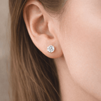 Close-up of an ear wearing a diamond stud earring with blurred hair and skin in the background