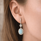 Close-up of an earring with a light blue gemstone and silver accents worn by a person.