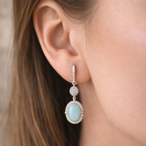 Close-up of an earring with a light blue gemstone and silver accents worn by a person.