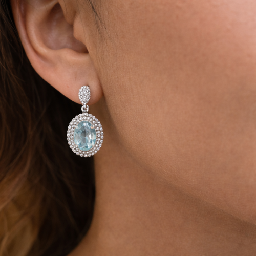 Close-up of a woman wearing a sparkling earring with a blue gemstone.