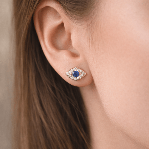 Close-up of an ear wearing a gold earring with a blue gemstone.