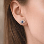 Close-up of an ear wearing a gold earring with a blue gemstone.