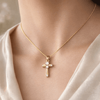 Gold cross necklace with a diamond pendant on a person wearing a beige top.