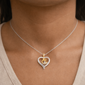 Necklace with a heart-shaped pendant featuring a gold and silver design on a person's neck.