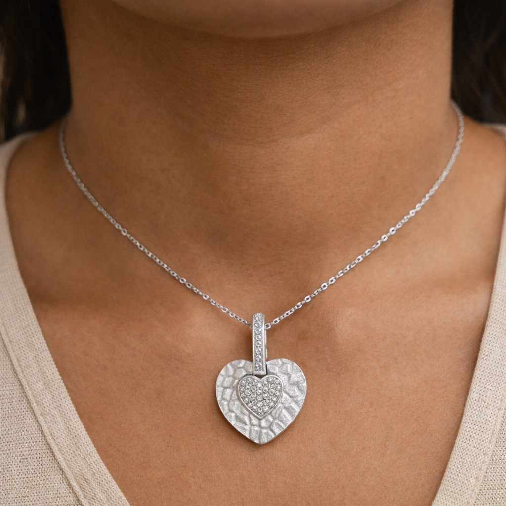 Silver heart-shaped pendant necklace on a person wearing a beige top.