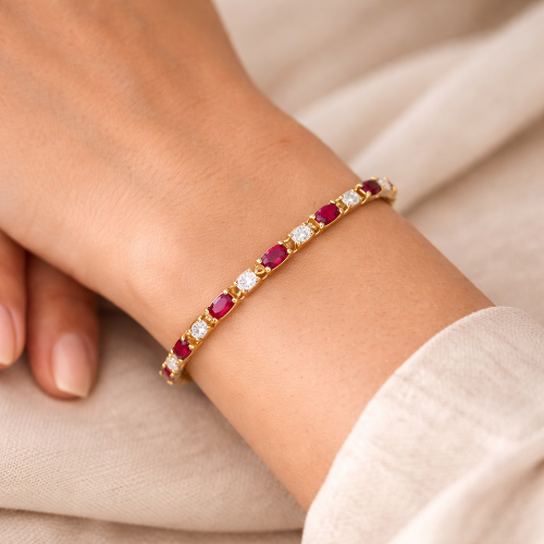 Gold bracelet with red and clear gemstones on a wrist against a beige background