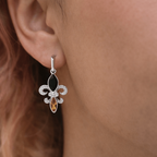 Silver earring with black and orange gemstones worn by a person with brown hair.