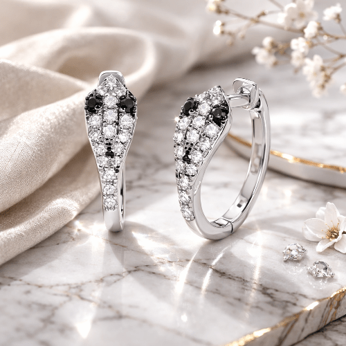 Silver earrings with black and white gemstones on a marble surface with flowers.