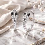 Silver earrings with black and white gemstones on a marble surface with flowers.