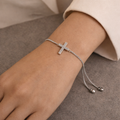 Silver bracelet with a cross charm on a wrist against a neutral background