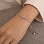 Silver bracelet with a cross charm on a wrist against a neutral background