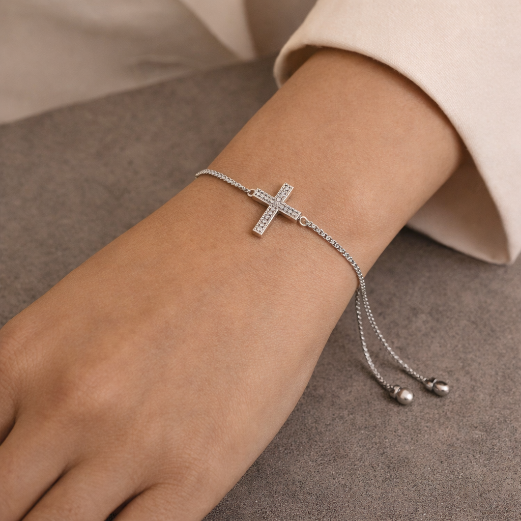 Silver bracelet with a cross charm on a wrist against a neutral background