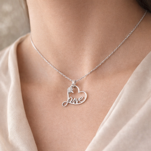Silver necklace with a heart-shaped 'love' pendant on a person wearing a beige top.