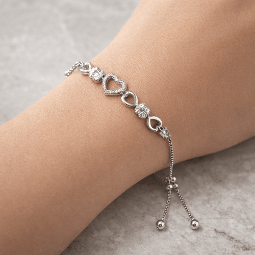 Silver bracelet with heart and bead details on a wrist against a neutral background